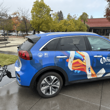 Minivan azul con calcomanía de Silicon Valley Hopper y portabicicletas en la parte trasera