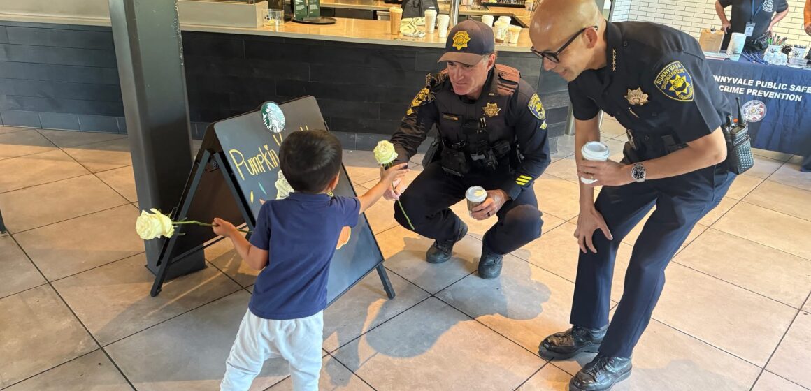 Phan Ngo, a bald tan Asian man wearing glasses and a Public Safety Officer uniform, squatting beside a tan child holding two yellow roses.