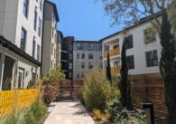 A sidewalk path leads to a gate in front of a five-story apartment building