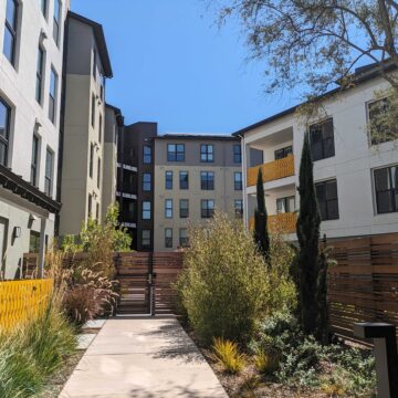 A sidewalk path leads to a gate in front of a five-story apartment building