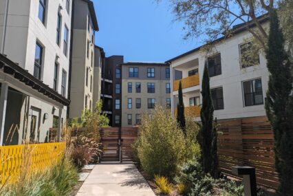 A sidewalk path leads to a gate in front of a five-story apartment building