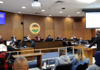 Photo of the Santa Clara City Council chambers with councilmembers sitting at their dias and City Manager Jovan Grogan, a tall Black man in a suit, giving a presentation