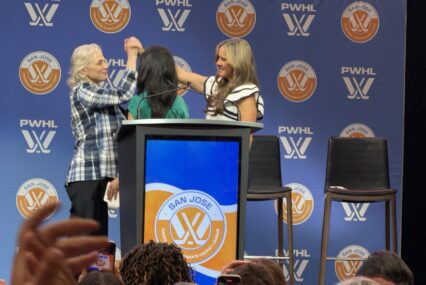 Three women clasp hands on a stage