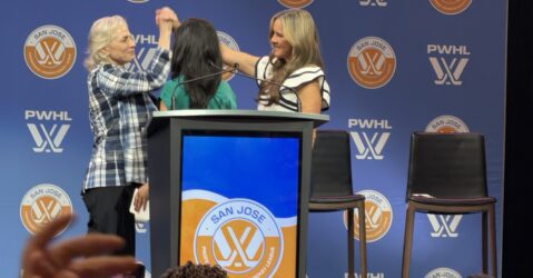 Three women clasp hands on a stage