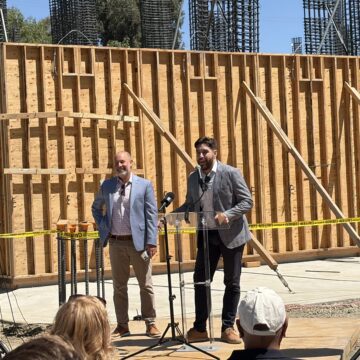 Two men speak to an audience at a construction site in Santa Clara, California